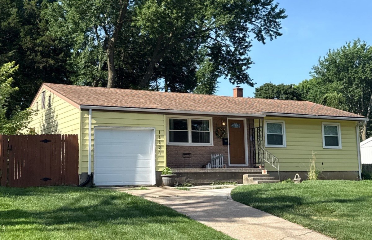 Yellow ranch-style house with brick accents, attached garage, and a well-maintained lawn under mature trees